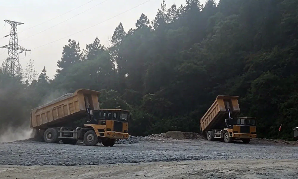 Two mining trucks on an unpaved road through wooded terrain.