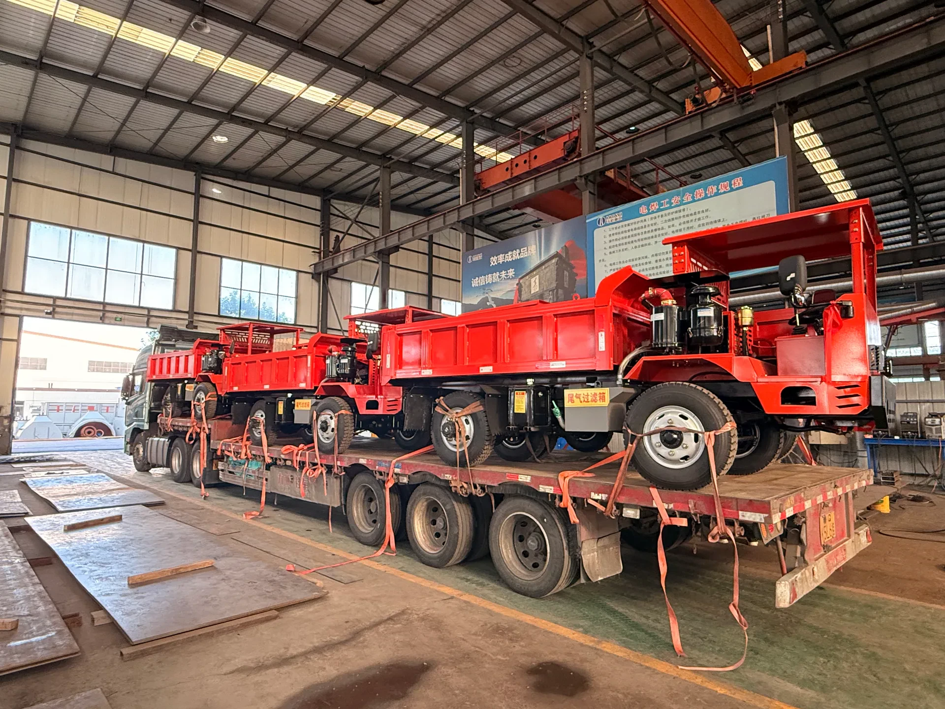 Red mining trucks placed on flatbed trailers inside a workshop.