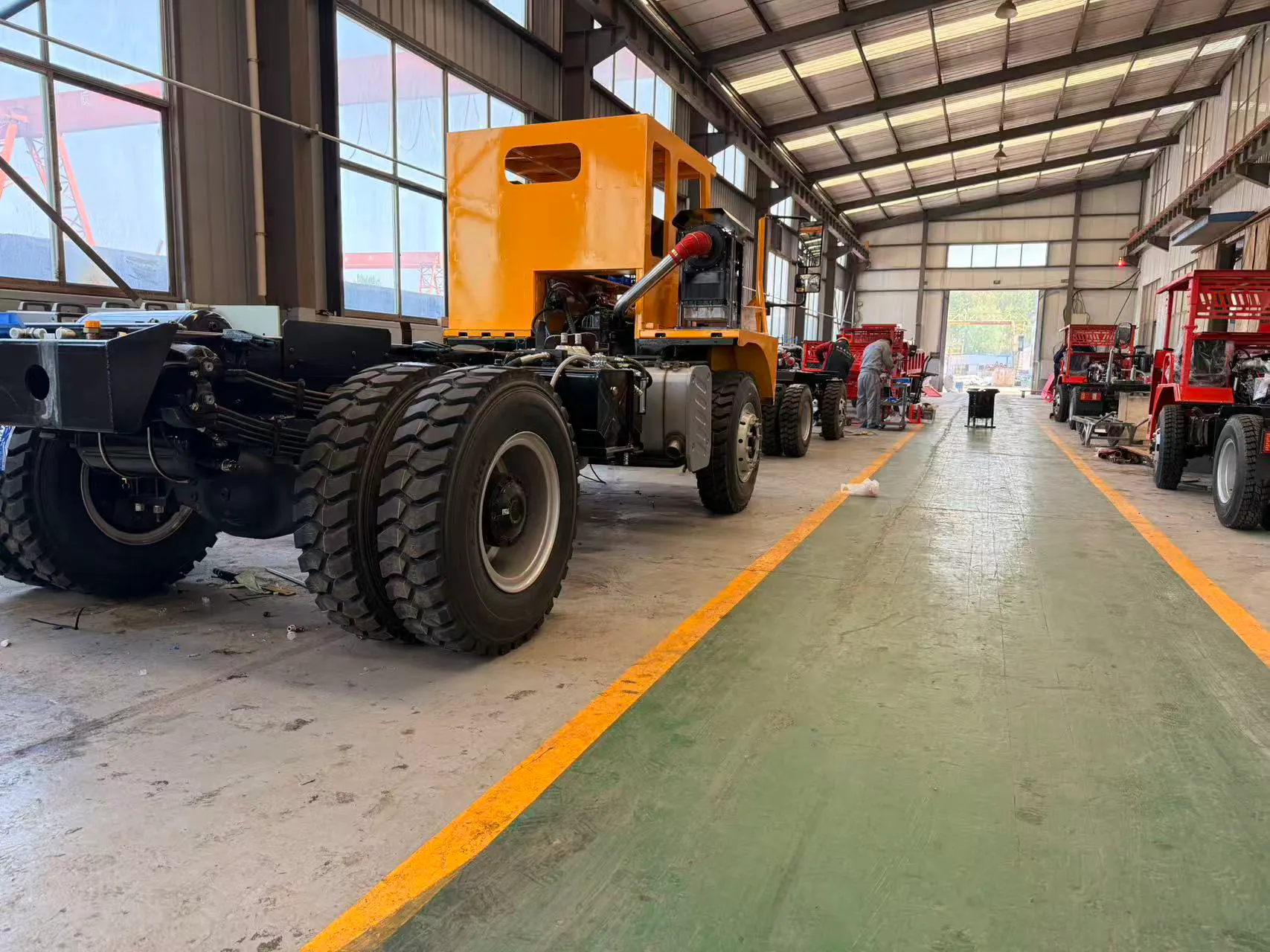 A yellow mining truck chassis and rear wheel inside a workshop.