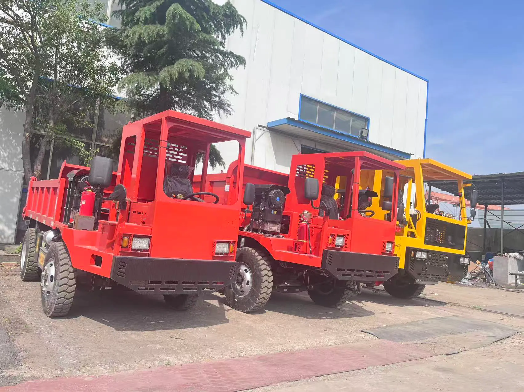 Red and yellow mining dump trucks arranged outside a workshop.
